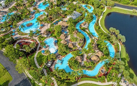 A large, landscaped resort with multiple swimming pools, palm trees, and a lake.