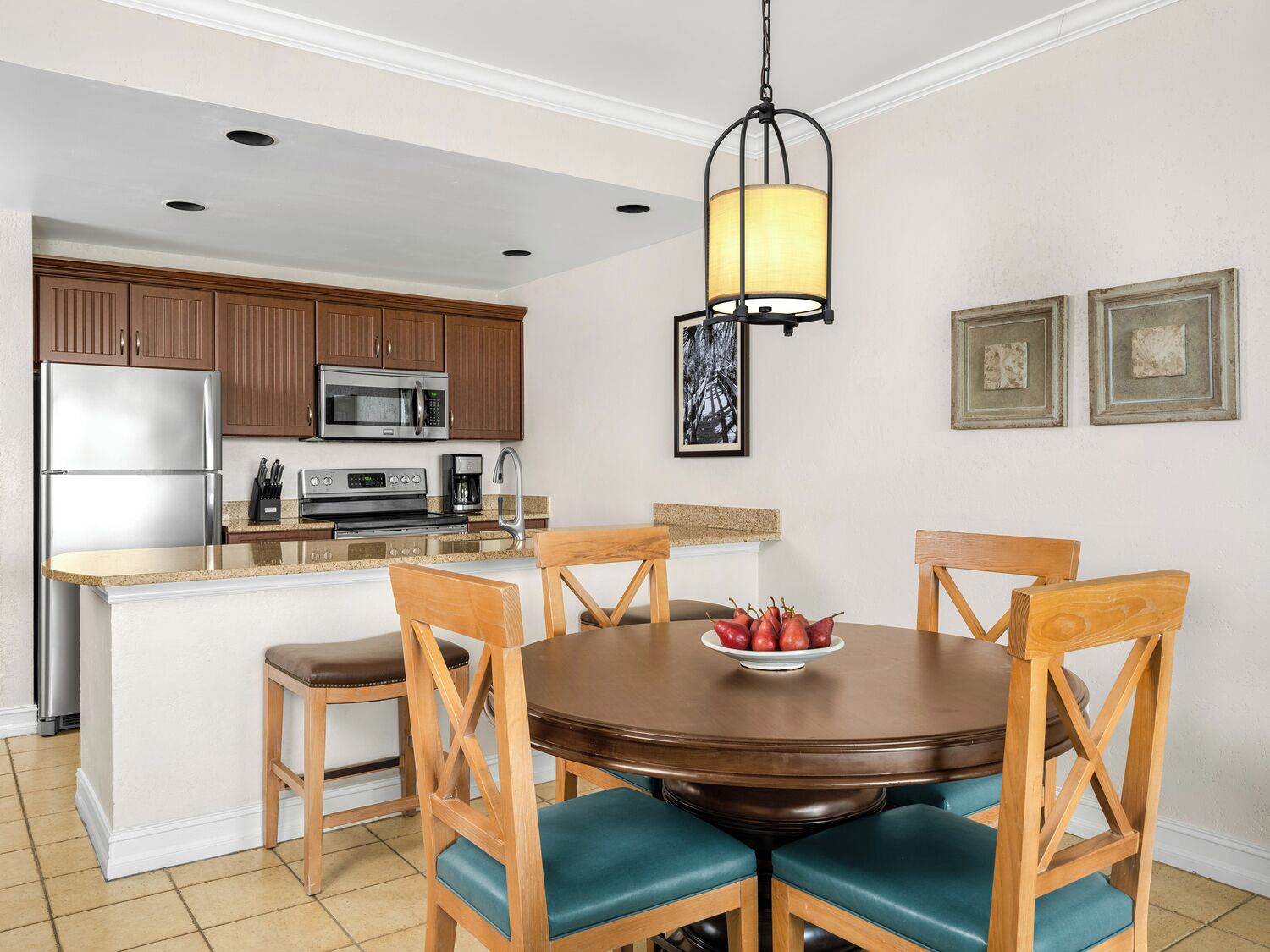 A modern kitchen with wooden cabinets, stainless steel appliances, and a round dining table with teal chairs.