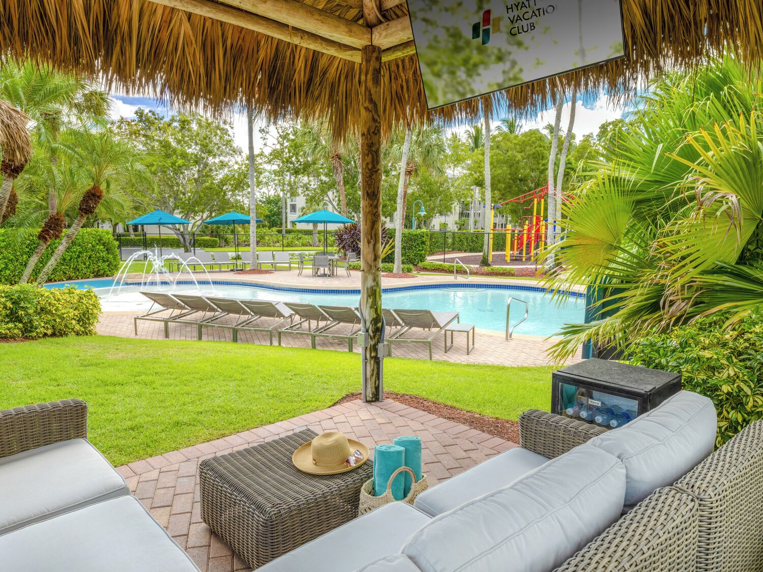A poolside area with lounge chairs, a thatched roof, and a sign for the Hyatt Vacation Club.
