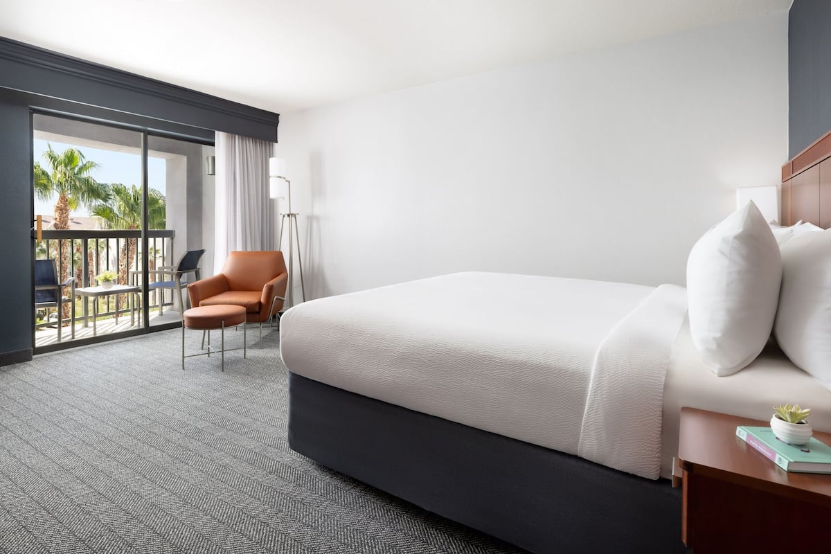 Ein Hotelzimmer mit einem Bett, einem Sessel, einem Nachttisch und Blick ins Freie.