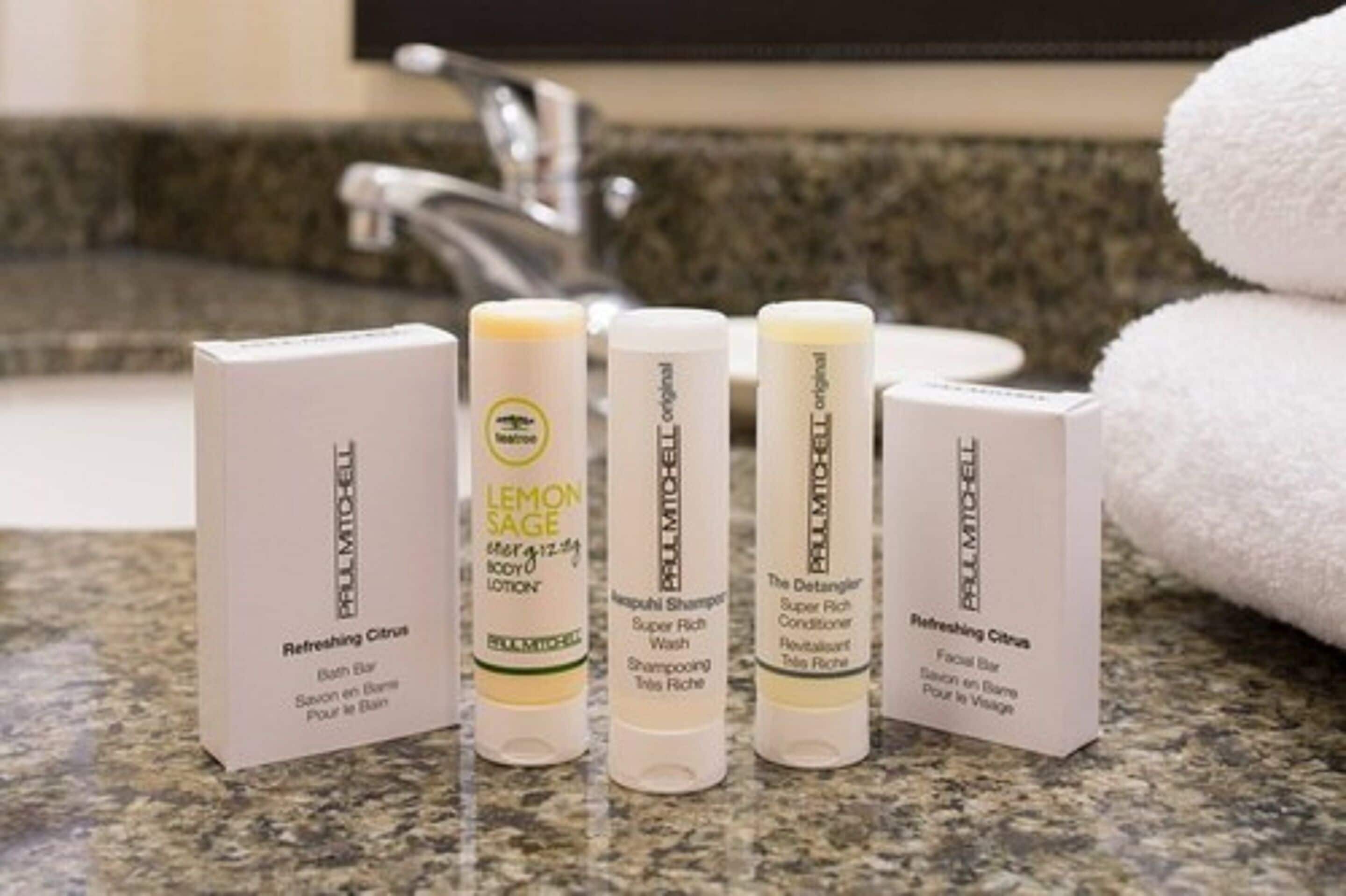 Un meuble de salle de bain sur lequel sont posées cinq bouteilles de produits PALLMICOE, dont un savon rafraîchissant aux agrumes, une lotion pour le corps au citron et à la sauge, un shampooing très nourrissant et un savon pour le visage.