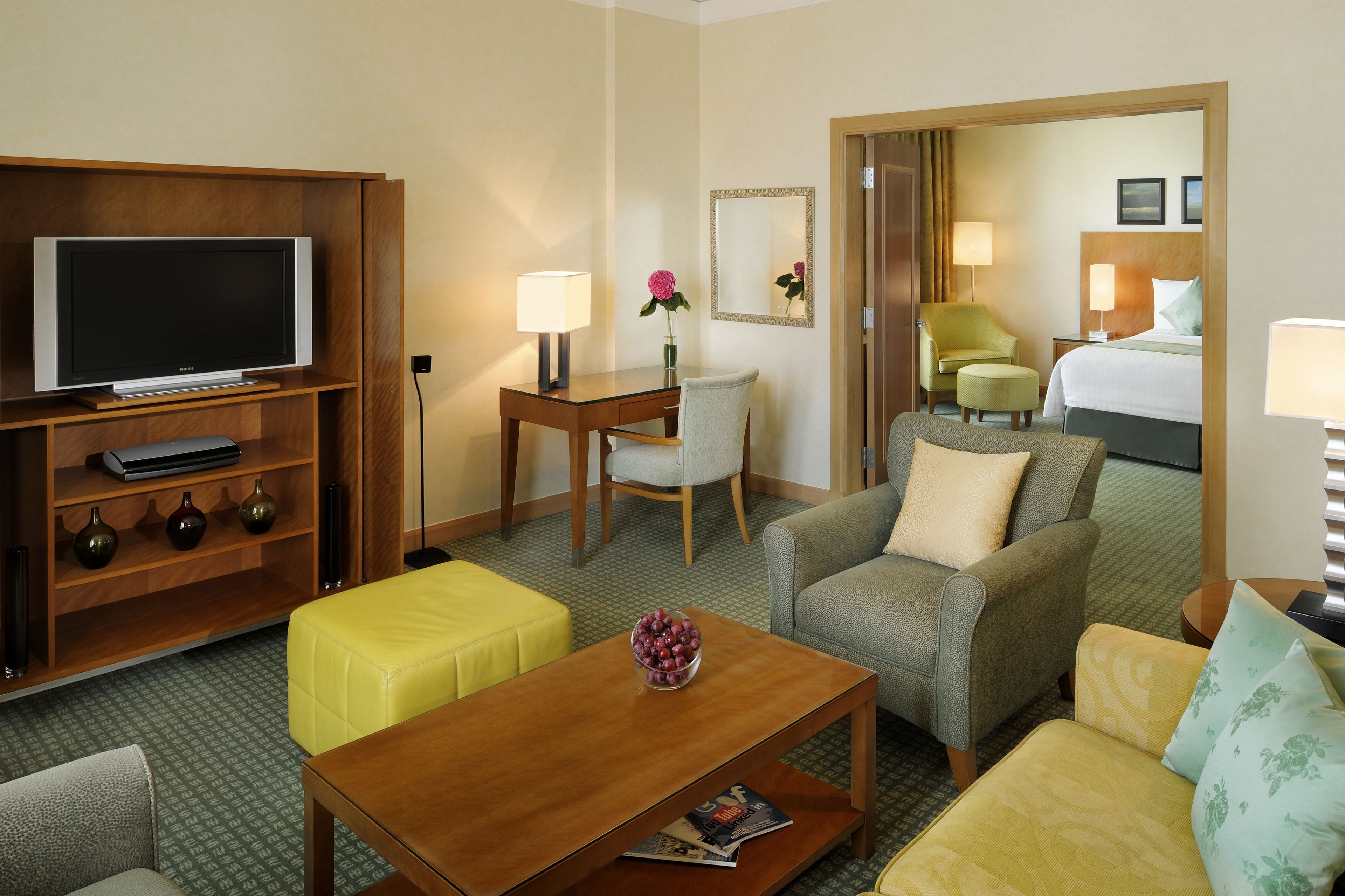 A hotel room with a television, a desk with a lamp, a chair, a sofa, and a bed.