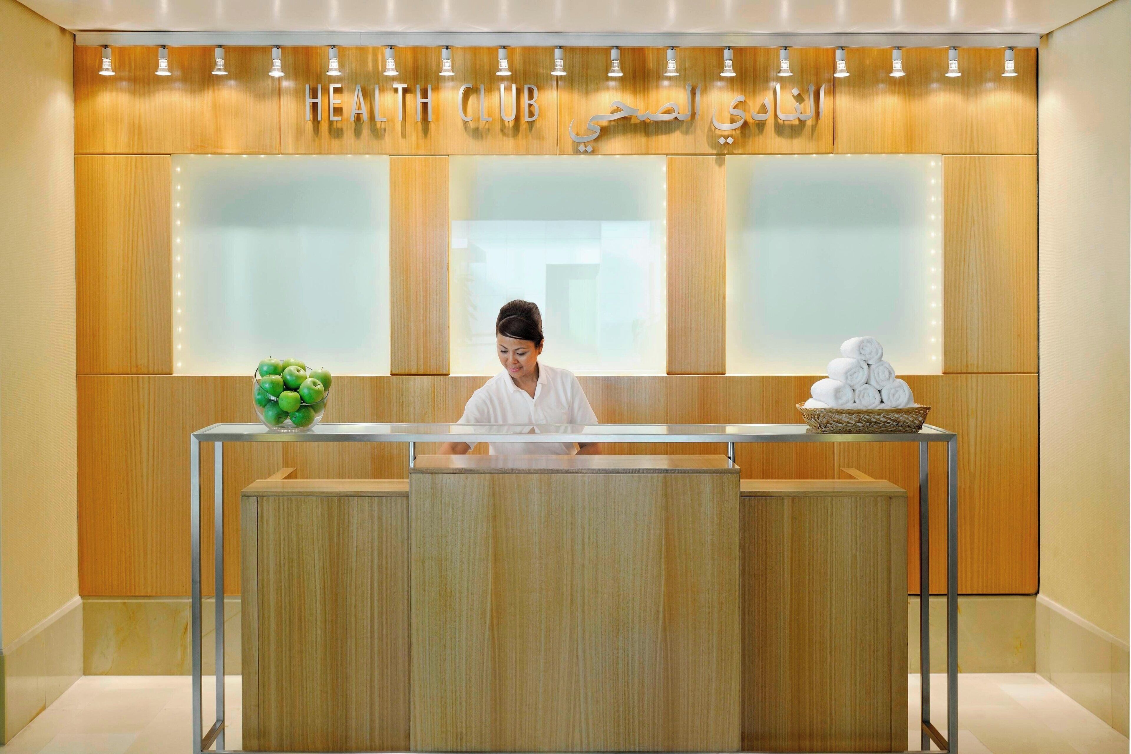 A reception desk with a wooden finish, a glass partition, and a sign above reading "HEALTH CLUB".