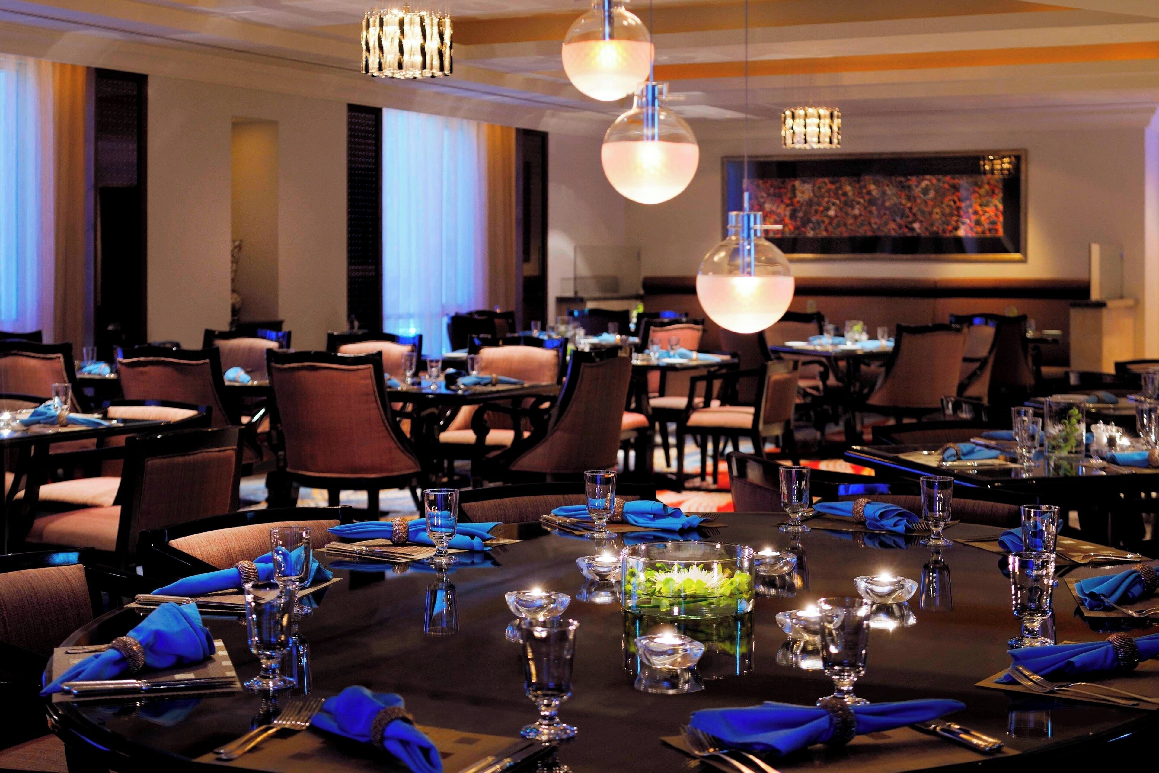 A restaurant with round tables set for dining, featuring blue napkins and clear glassware.