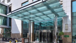 L’entrée d’un hôtel, dotée d’un auvent en verre, d’une porte tournante et d’un espace détente avec des chaises et une table.