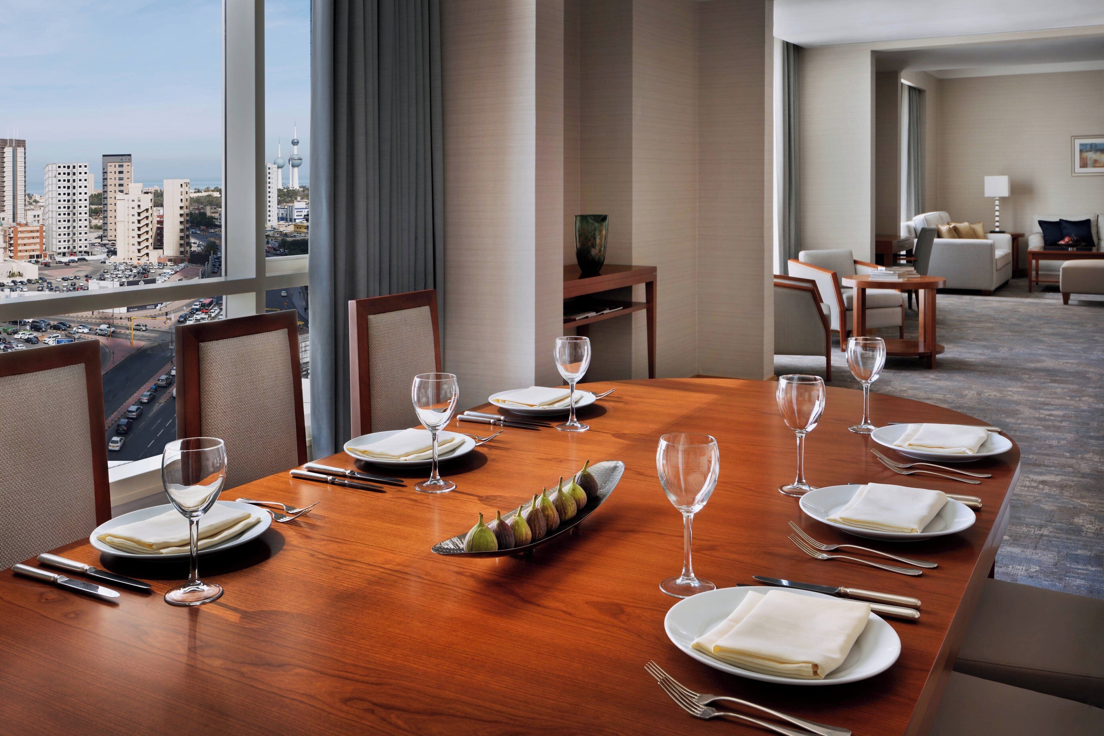 Mesa de jantar posta para seis pessoas com vista para a cidade, uma mesinha de madeira e um sofá ao fundo.