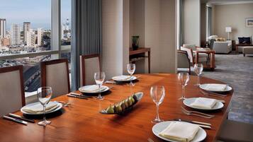 Mesa de jantar posta para seis pessoas com vista para a cidade, uma mesinha de madeira e um sofá ao fundo.