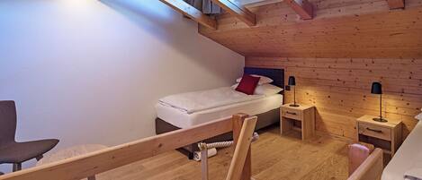 Une petite pièce agréable, dotée d’un lit en mezzanine, d’un bureau et d’une chaise.