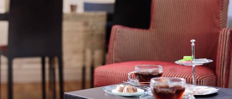 A cozy seating area with a red upholstered chair, a small table with a glass of tea, a plate of pastries, and a glass of red beverage.