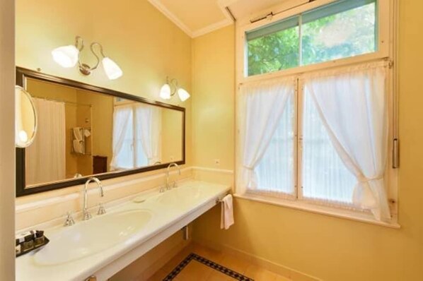 A bathroom with two sinks, a large mirror, and a window with sheer curtains.