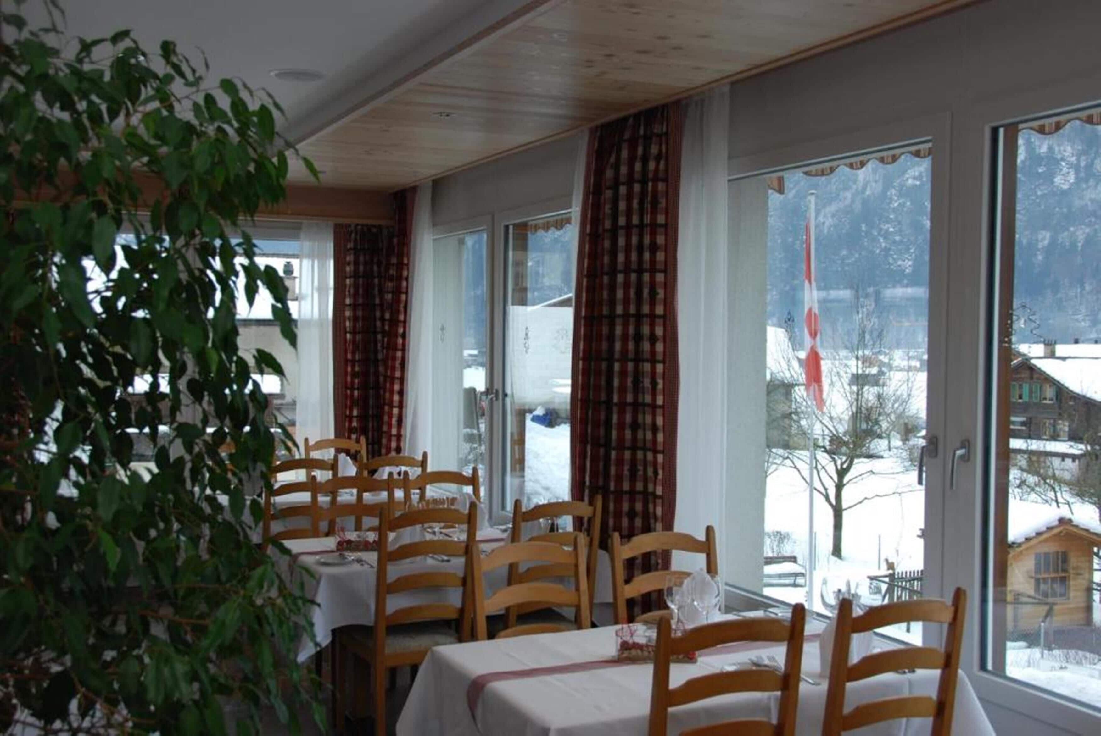 A dining area with wooden chairs and tables, large windows with curtains, and a view of a snowy landscape.