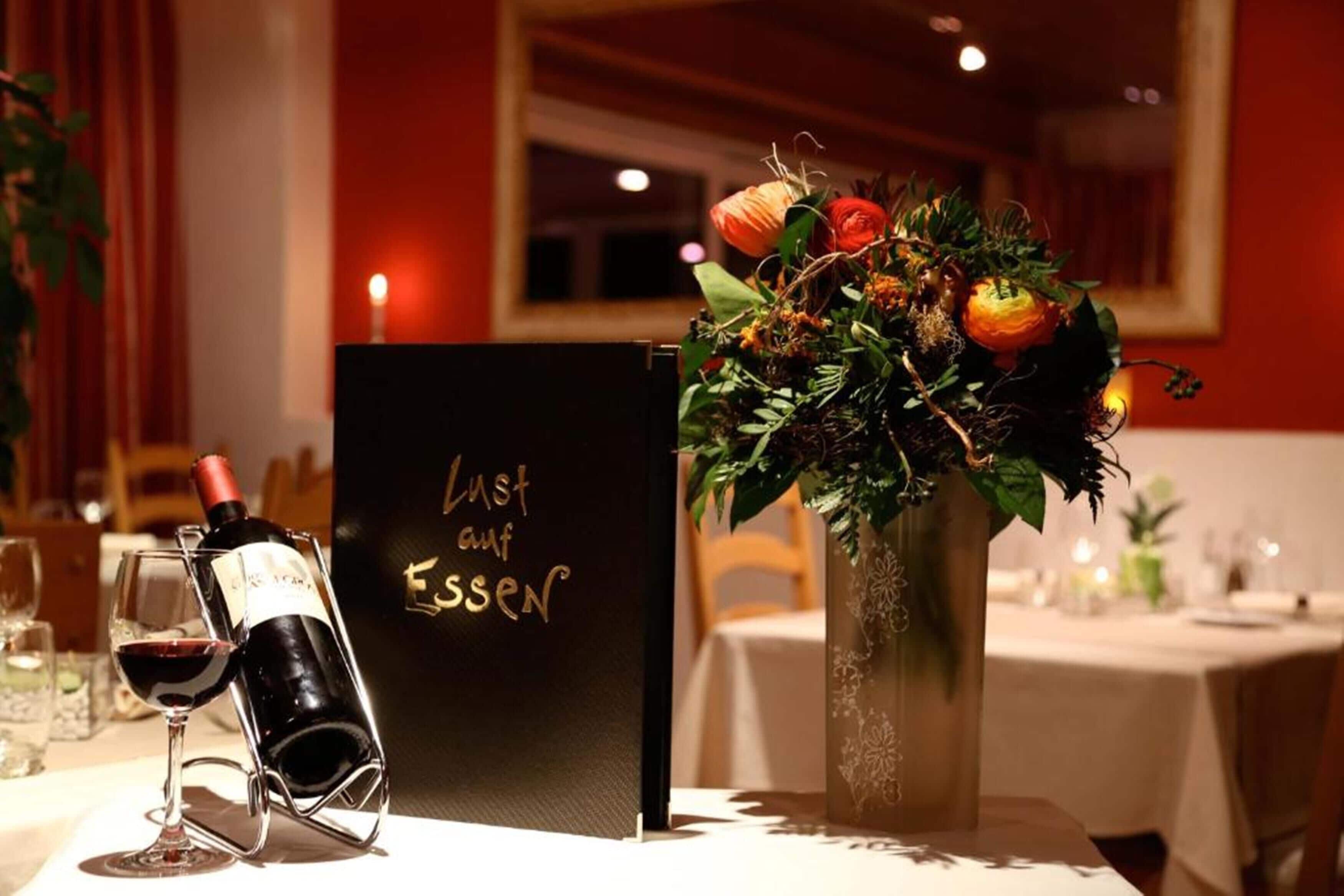 A table set with a wine bottle, a glass, a menu, and a floral centerpiece.