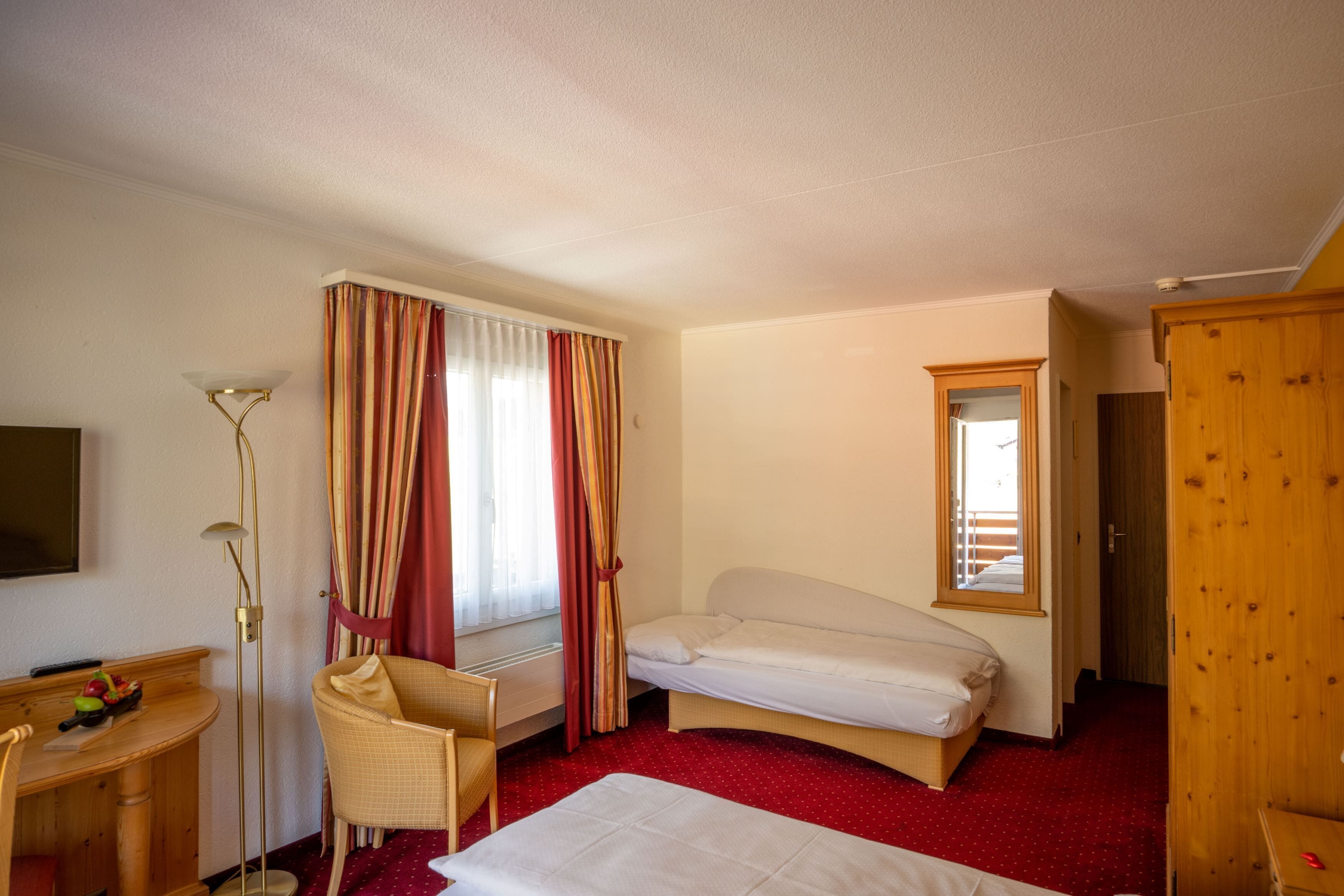 Una habitación de hotel con una cama individual, un escritorio con una silla, una mesita con un frutero, y un armario.