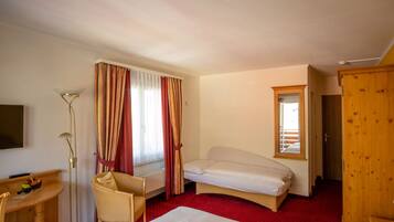 Una habitación de hotel con una cama individual, un escritorio con una silla, una mesita con un frutero, y un armario.