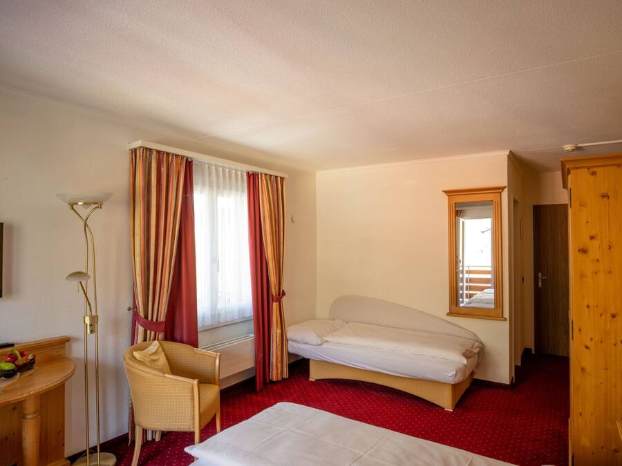 Una habitación de hotel con una cama individual, un escritorio con una silla, una mesita con un frutero, y un armario.
