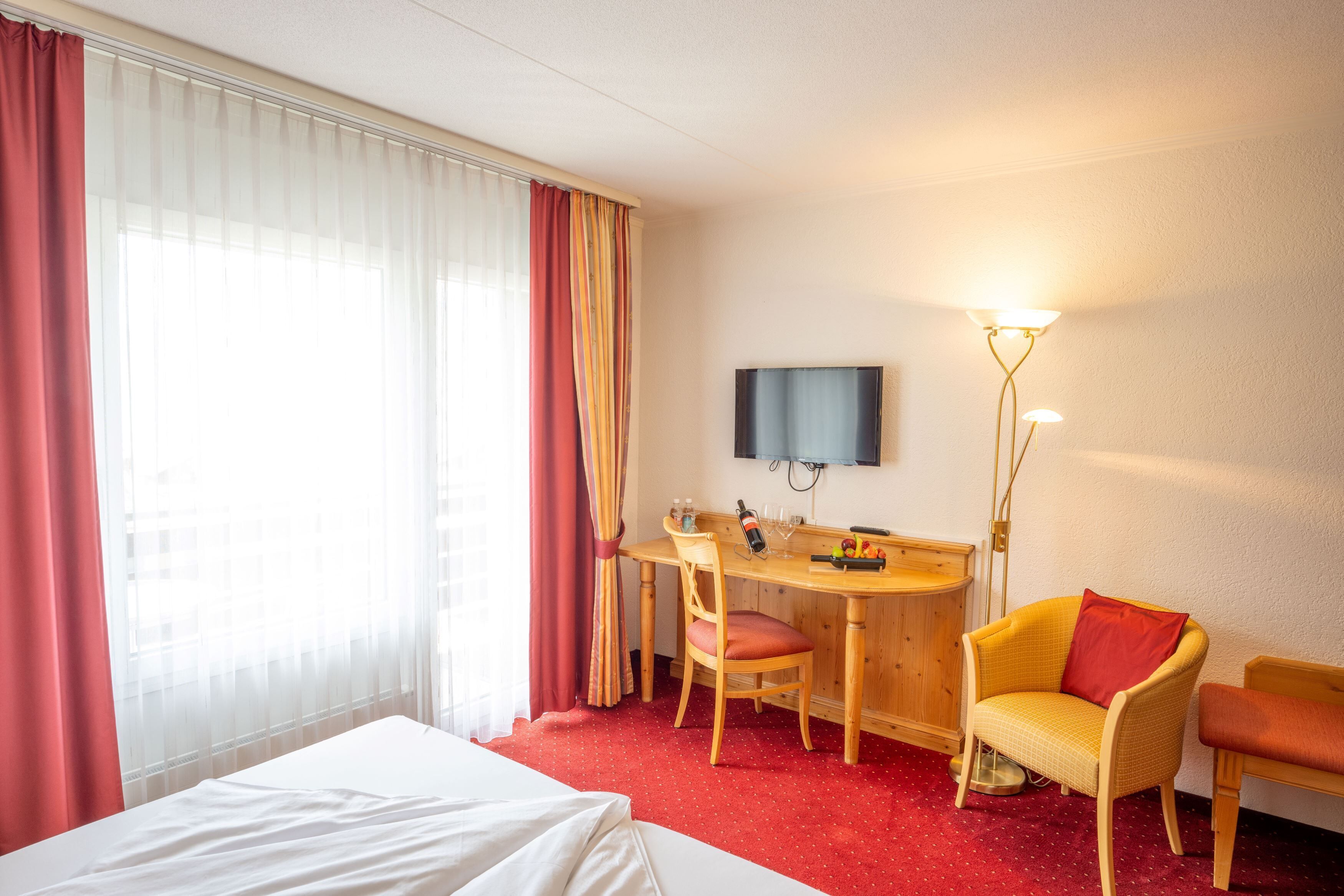 Una habitación de hotel con una cama, un escritorio con una silla, un televisor y una lámpara.