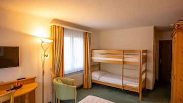 Ein Hotelzimmer mit Etagenbett, Schreibtisch, Stuhl, Lampe und einem Fenster mit Vorhängen.