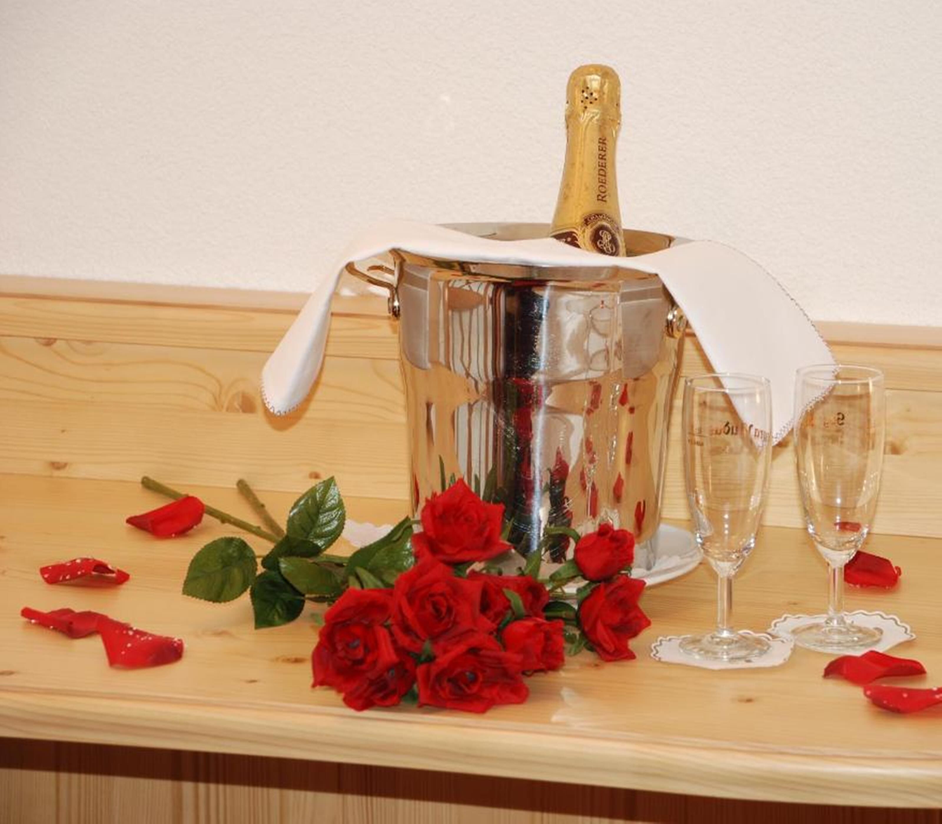 A champagne bucket with a white cloth, surrounded by red roses and empty champagne flutes on a wooden surface.