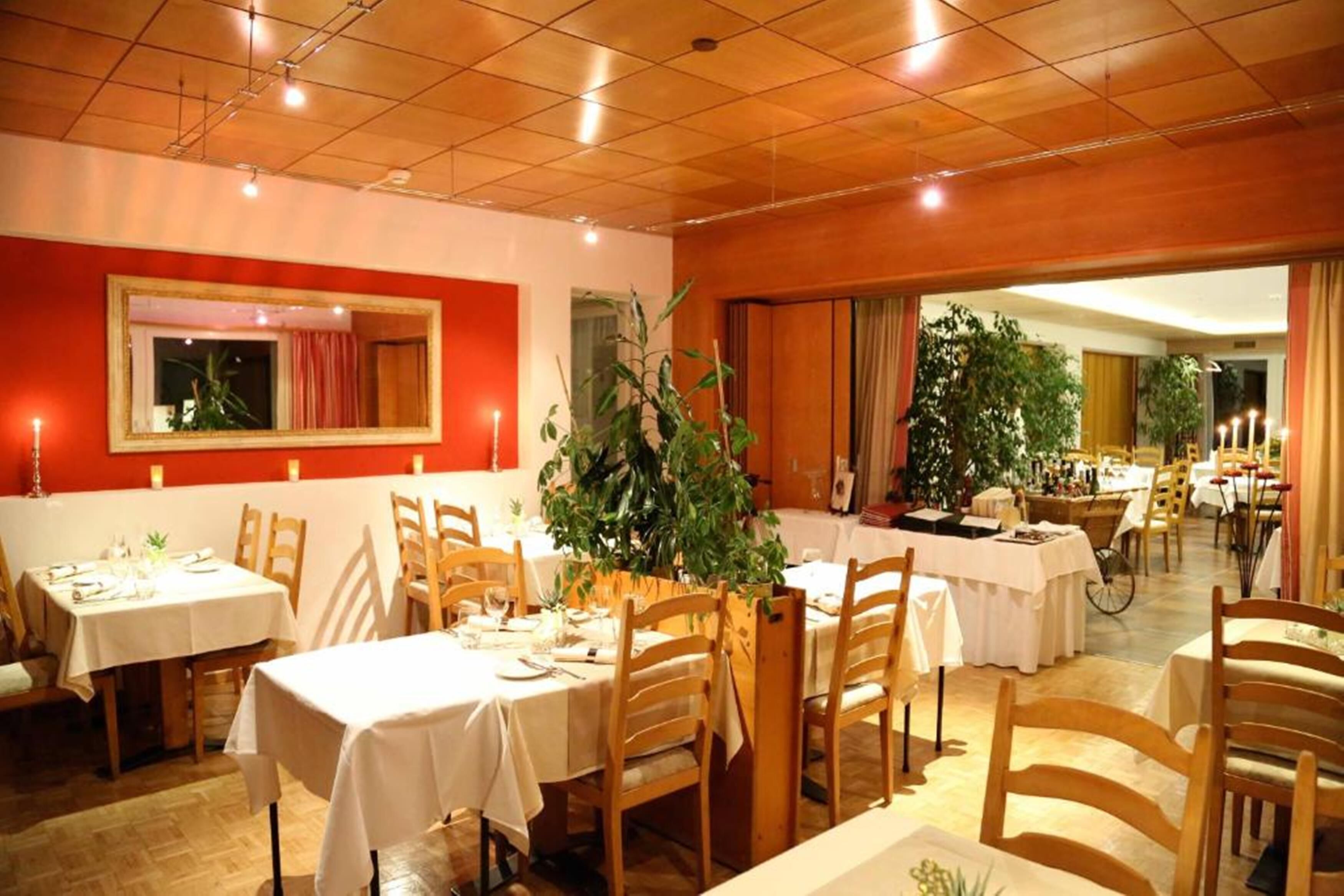 A restaurant with multiple tables and chairs, wooden flooring, and a warm color scheme.