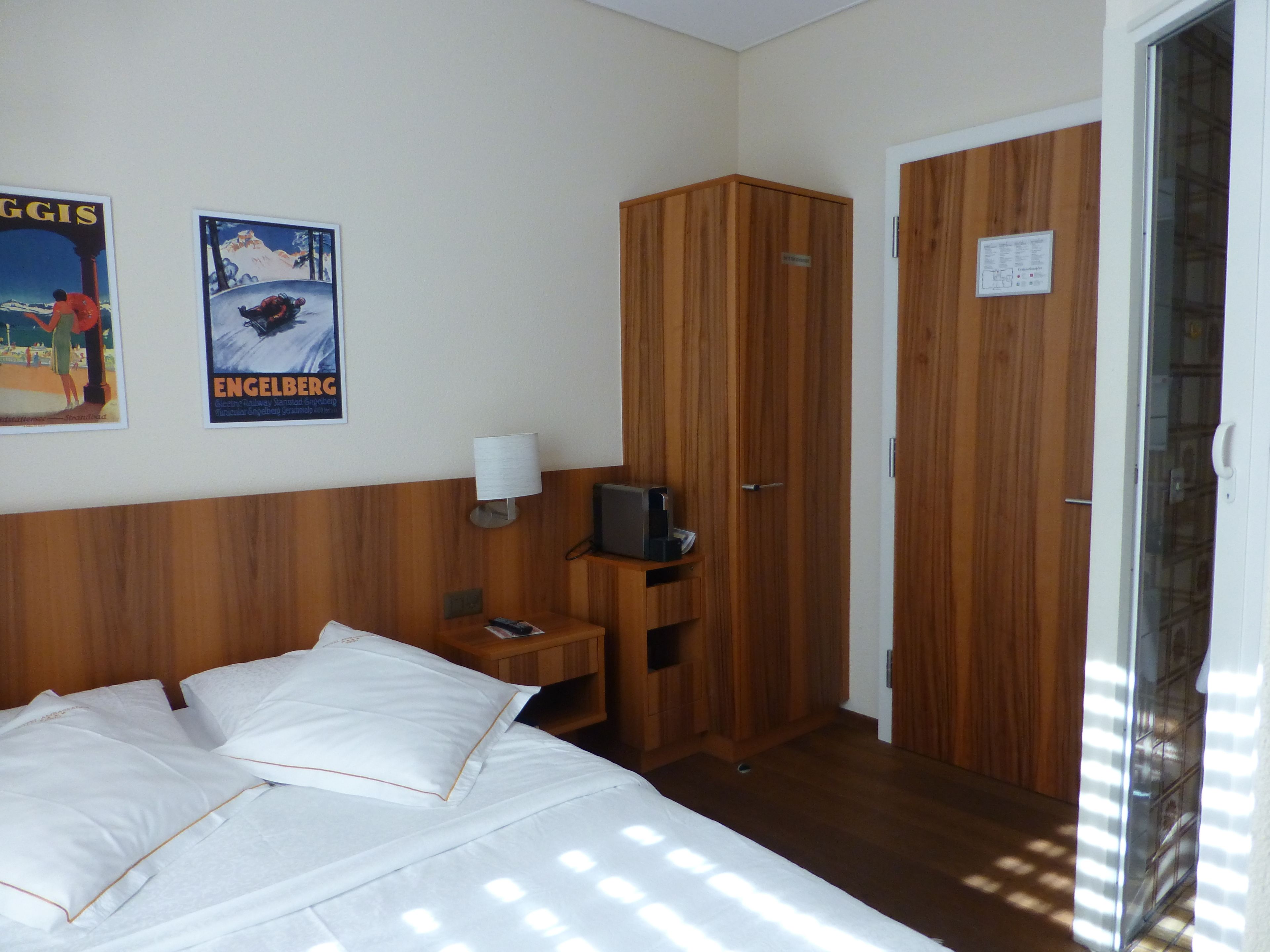 Une chambre d’hôtel avec un lit, une armoire en bois, une table de chevet avec une lampe et des affiches au mur.