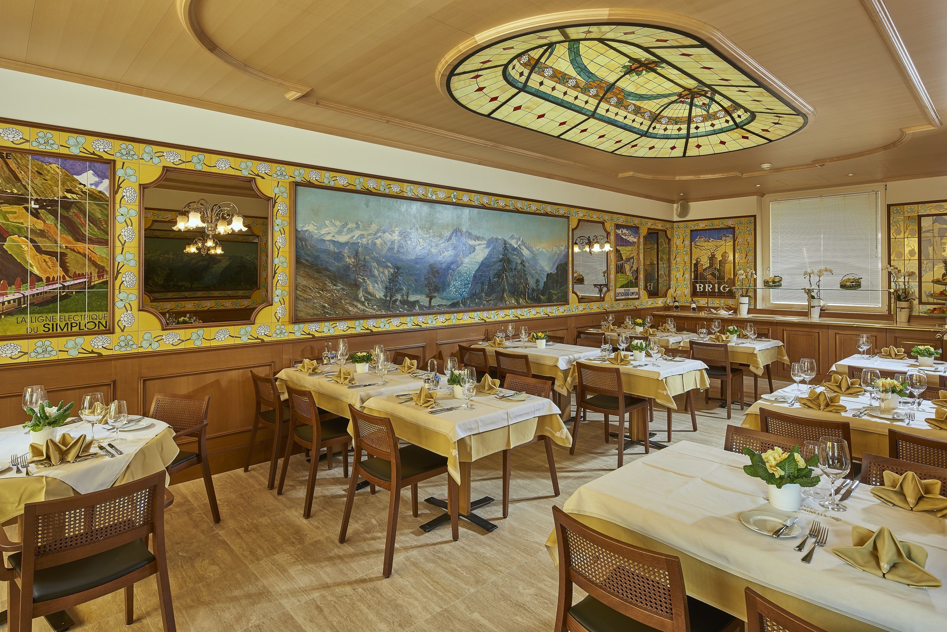 Un restaurante con varias mesas dispuestas para comer, que destaca por un amplio mural en la pared y un techo decorativo.