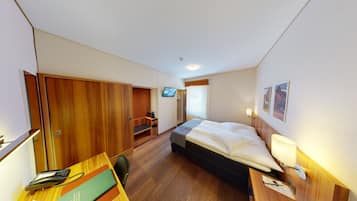 A hotel room with a bed, a desk with a phone and books, a TV, and a shower area.