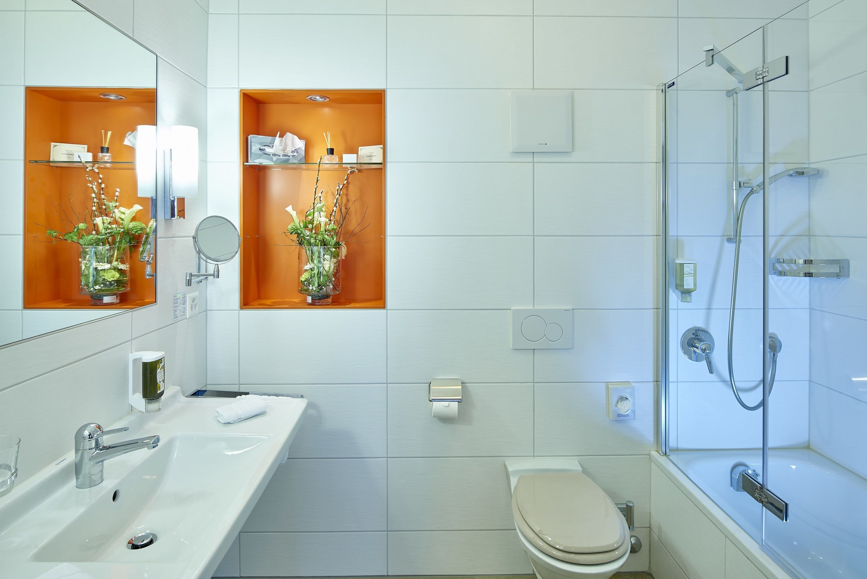 Une salle de bain moderne avec un lavabo blanc, un miroir et des toilettes. On y trouve deux cabines de douche en verre et une porte de douche en verre.