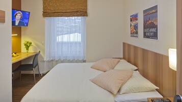 Une chambre d’hôtel avec un lit, un bureau, une chaise, une télévision et deux affiches au mur.