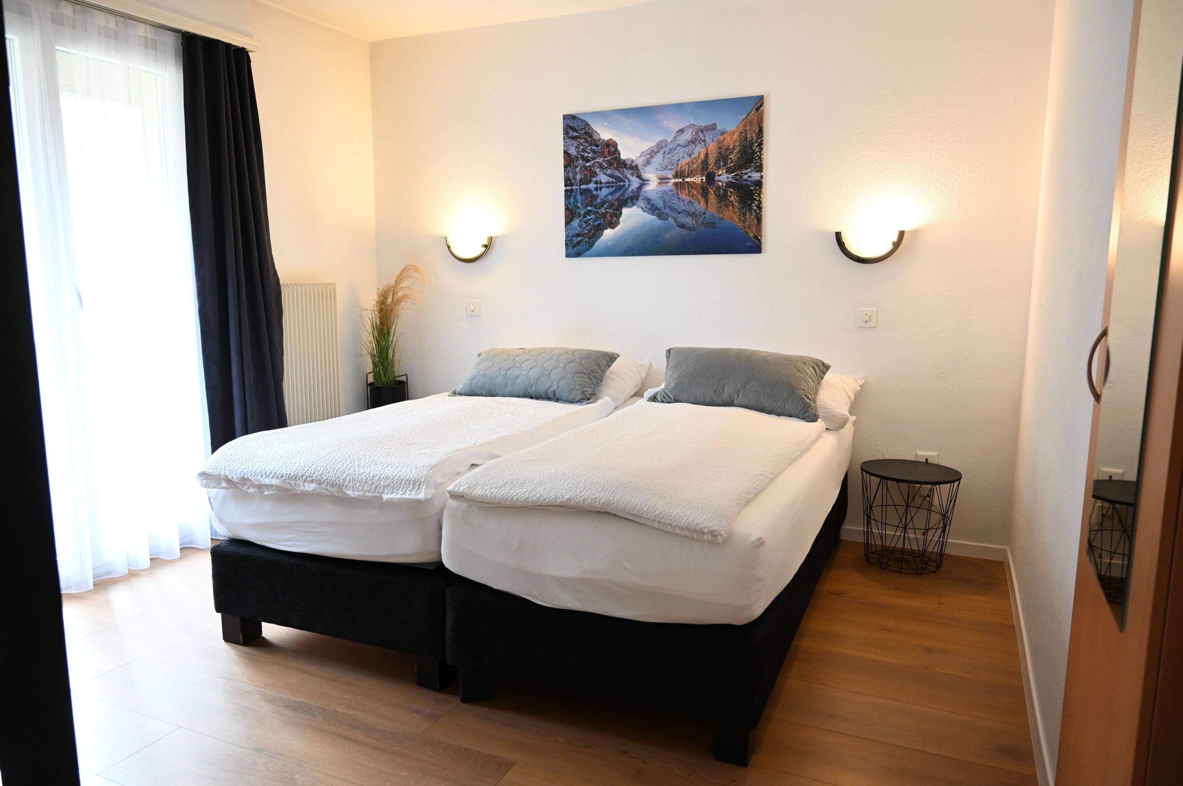 A double bed with white linens, a wall-mounted picture, and two wall sconces.