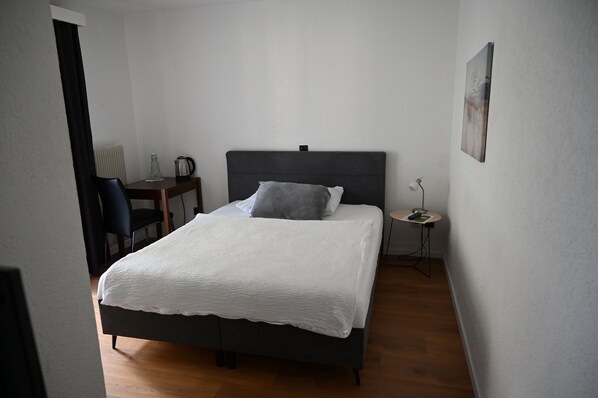 Une chambre à coucher avec un lit, une chaise, une petite table et une lampe.