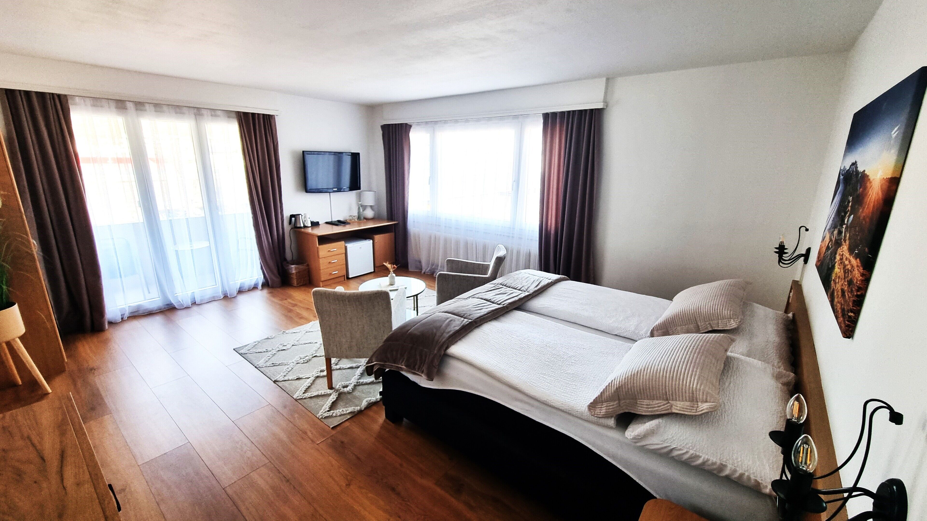 Habitación de hotel con cama, escritorio, silla, televisor y ventana con cortinas.