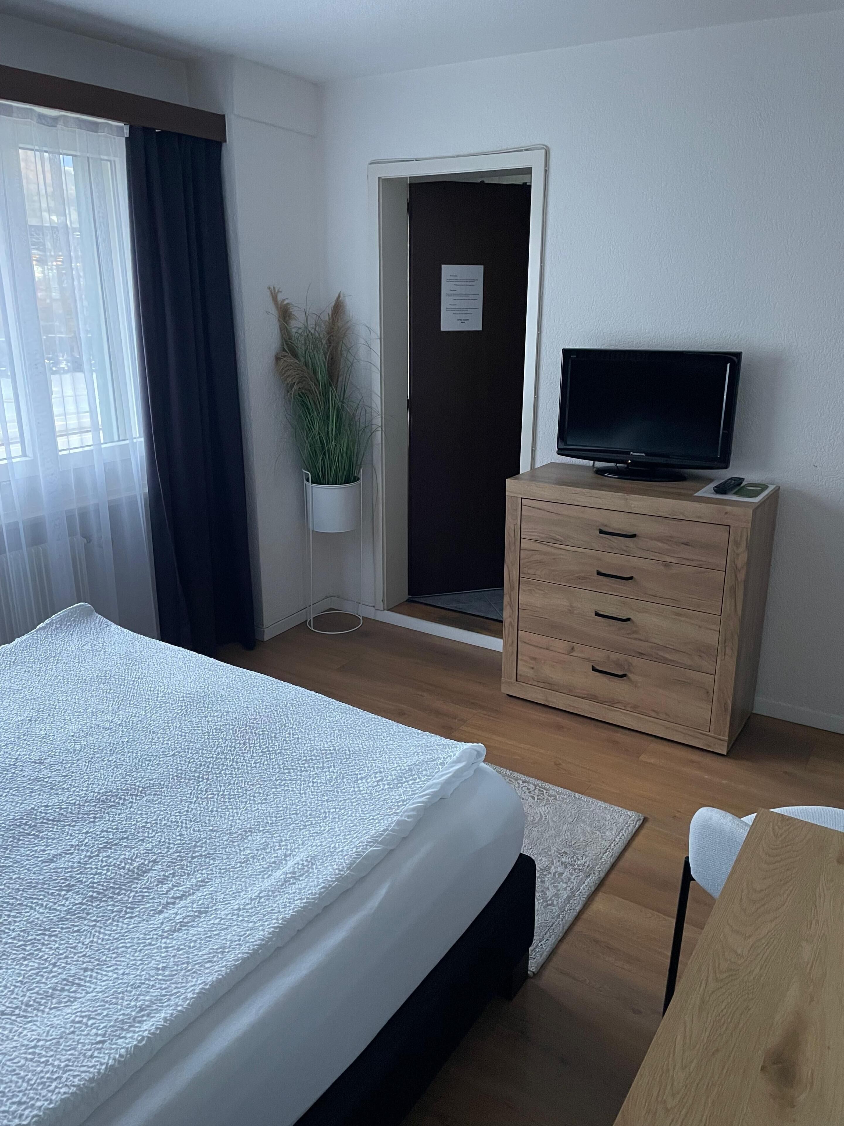 Une chambre d’hôtel avec un lit, une commode en bois, un téléviseur et une porte avec une pancarte.
