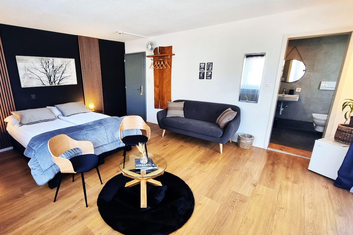 Un dormitorio moderno con cama, sofá, mesa redonda y espejo.