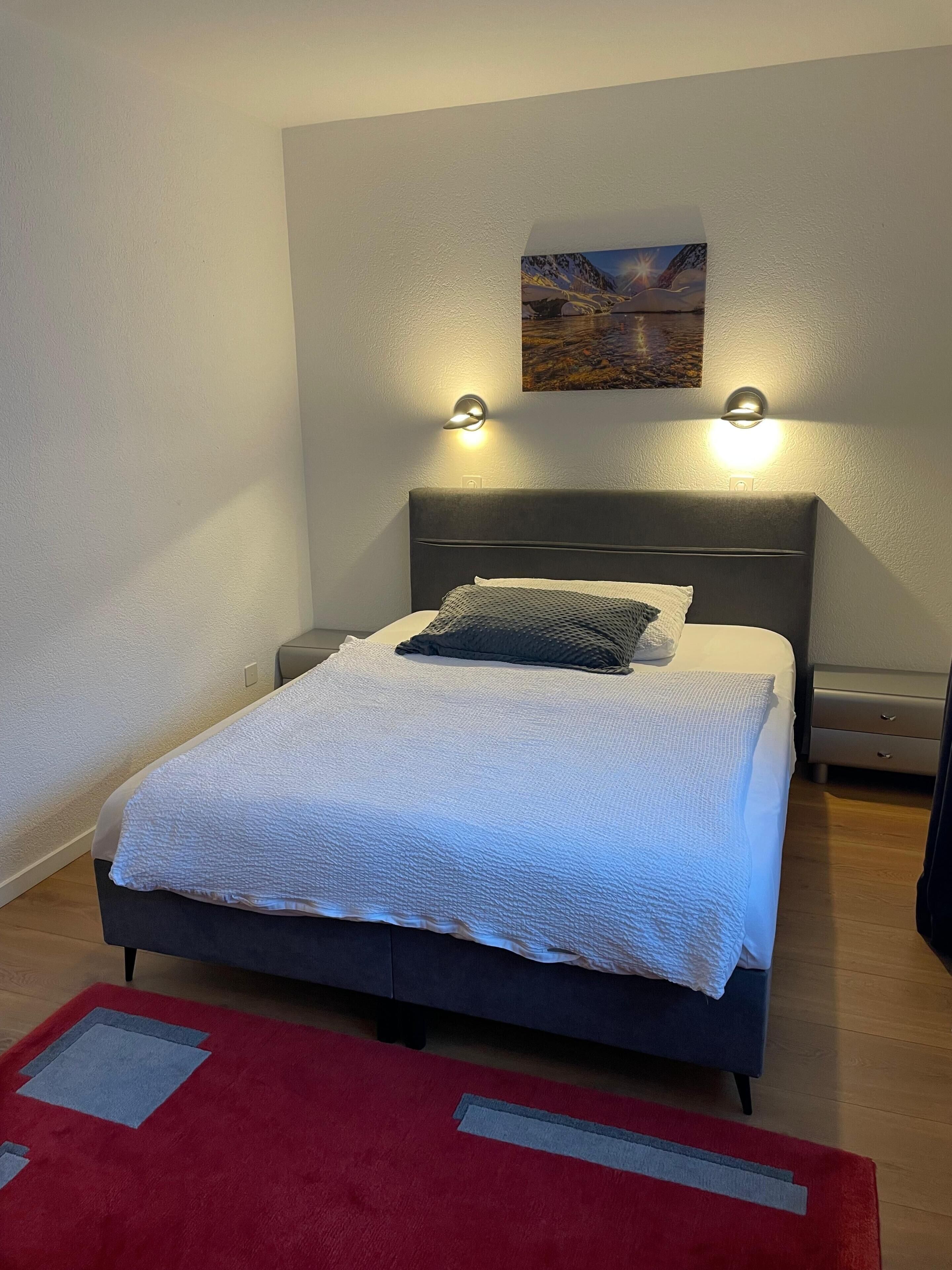 A bed with a white textured blanket, a dark headboard, and two wall-mounted lights.