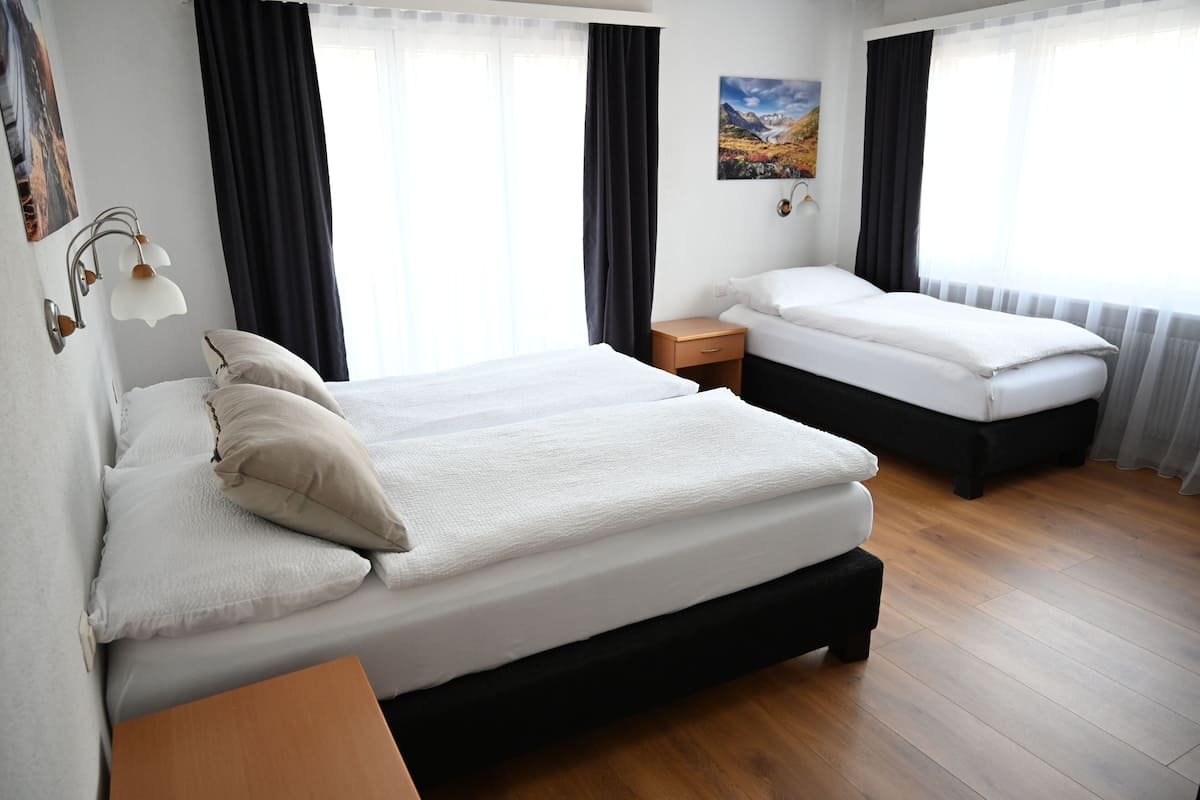 Habitación de hotel con dos camas, piso de madera, una mesita de noche, una lámpara y un cuadro en la pared.