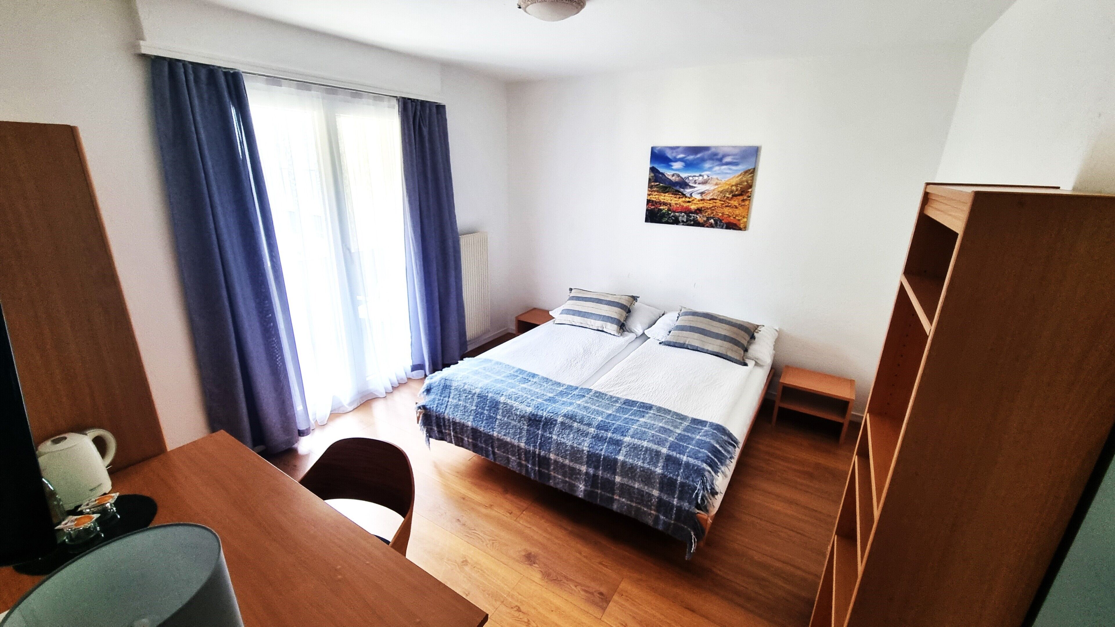 Une pièce comprenant un lit, un bureau, une chaise, une petite table et une fenêtre avec des rideaux.