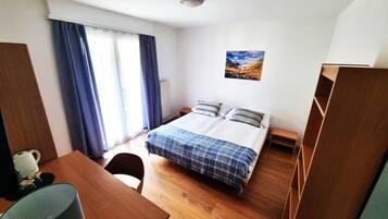Ein Zimmer mit einem Bett, einem Schreibtisch, einem Stuhl, einem kleinen Tisch und einem Fenster mit Vorhängen.