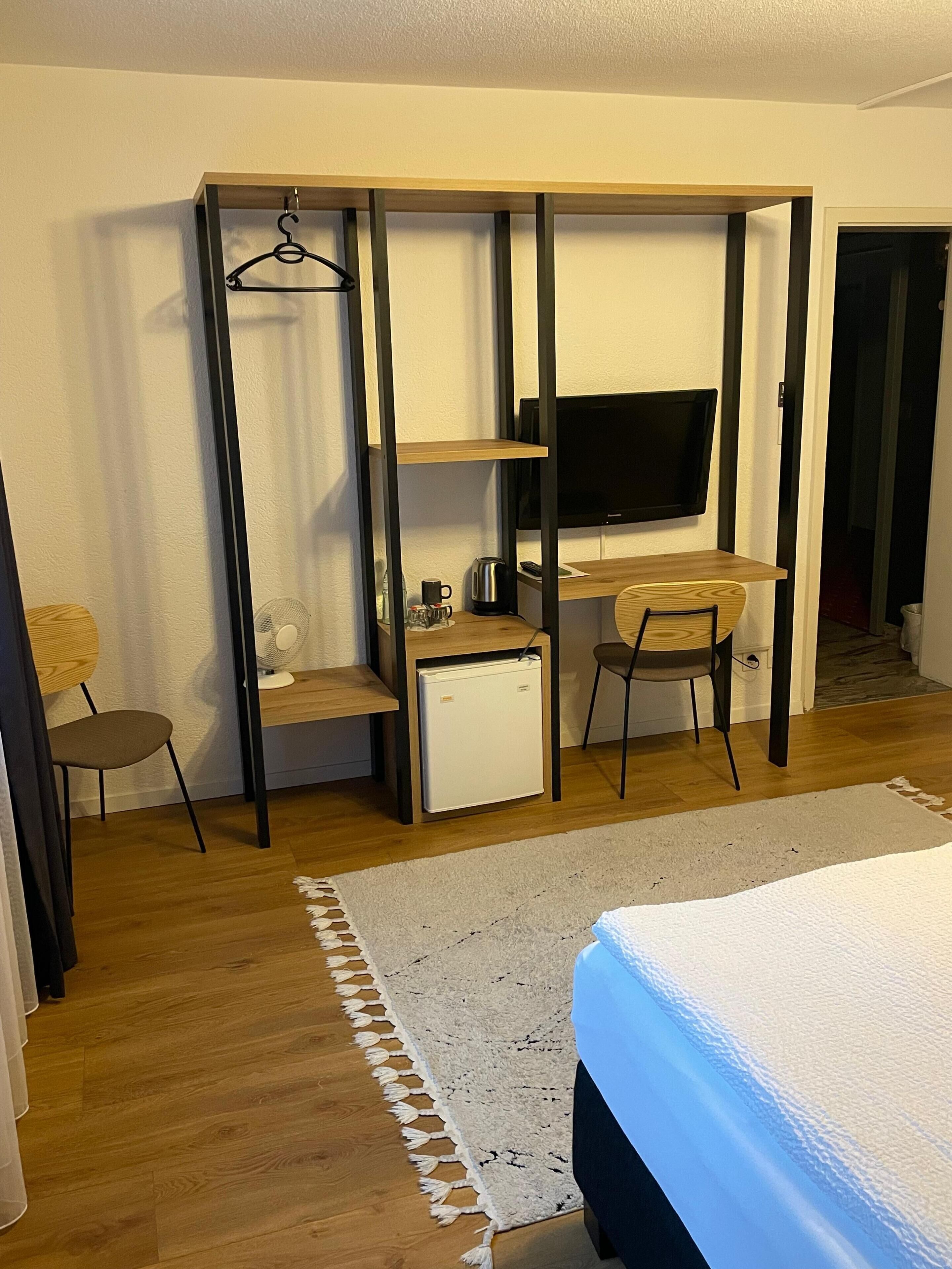 A compact room with a bed, a desk with a computer, a chair, a small fridge, and a TV.