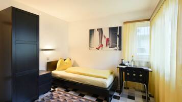 A hotel room with a bed, a desk, a chair, a wardrobe, and a painting on the wall.