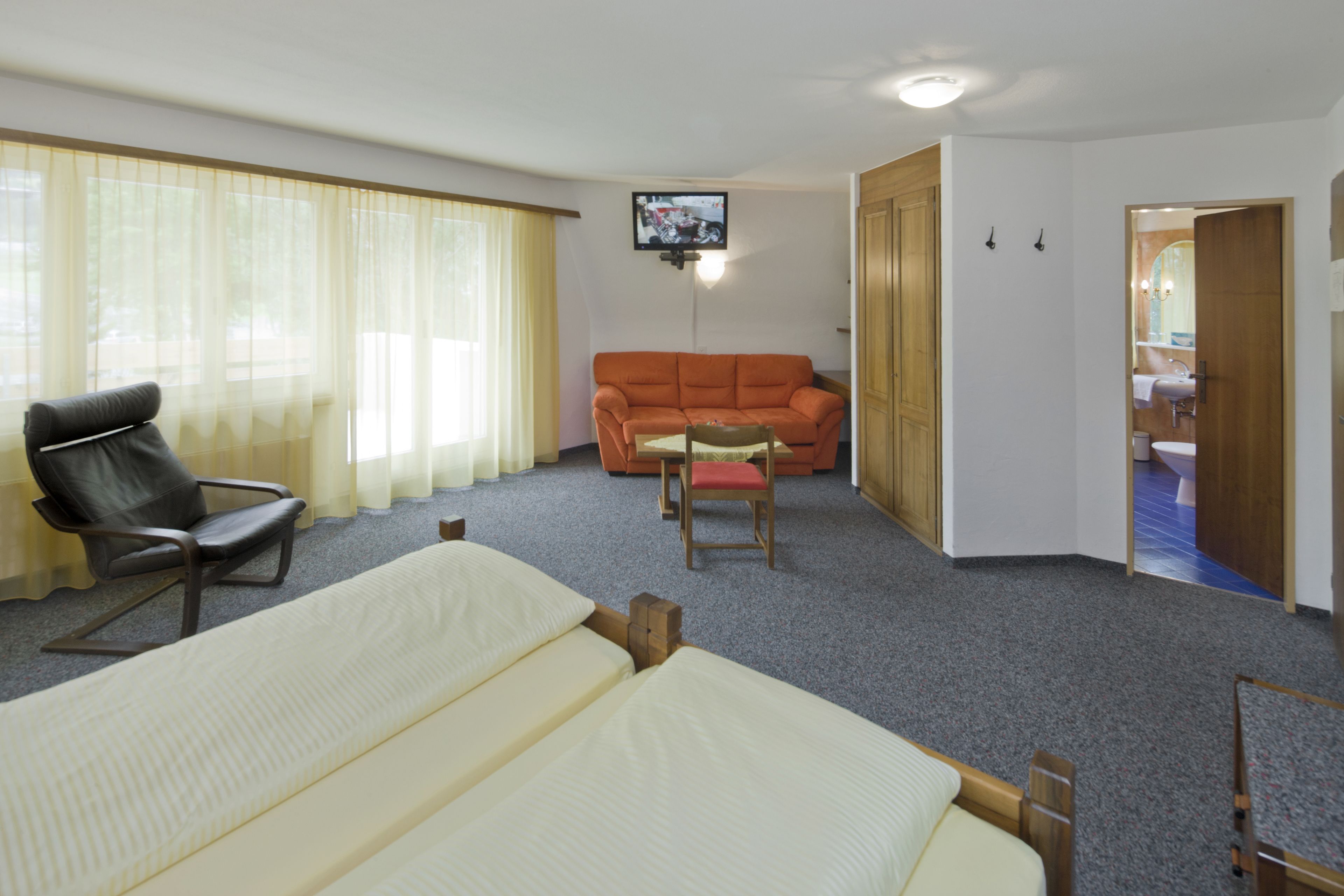 A hotel room with a bed, a chair, a sofa, and a television mounted on the wall.