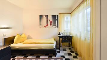 Una habitación de hotel con cama, escritorio, silla y ventana con cortinas.