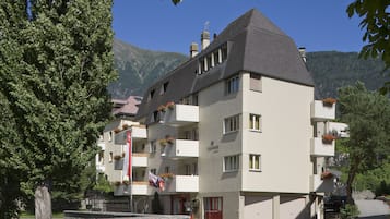 A multi-story hotel with balconies, a stone facade, and a mountain backdrop.