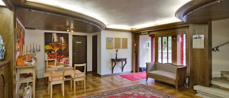 Een ruime woonkamer met een groot rood tapijt, houten meubels en een trap naar een verdieping.