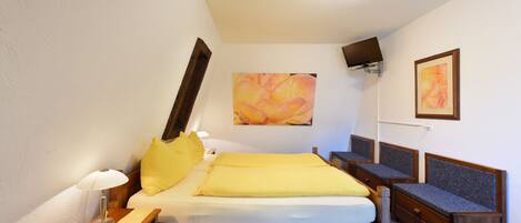 Une chambre à coucher comprenant un lit, des tables de chevet, une lampe, un téléviseur à écran plat fixé au mur et des œuvres d’art.