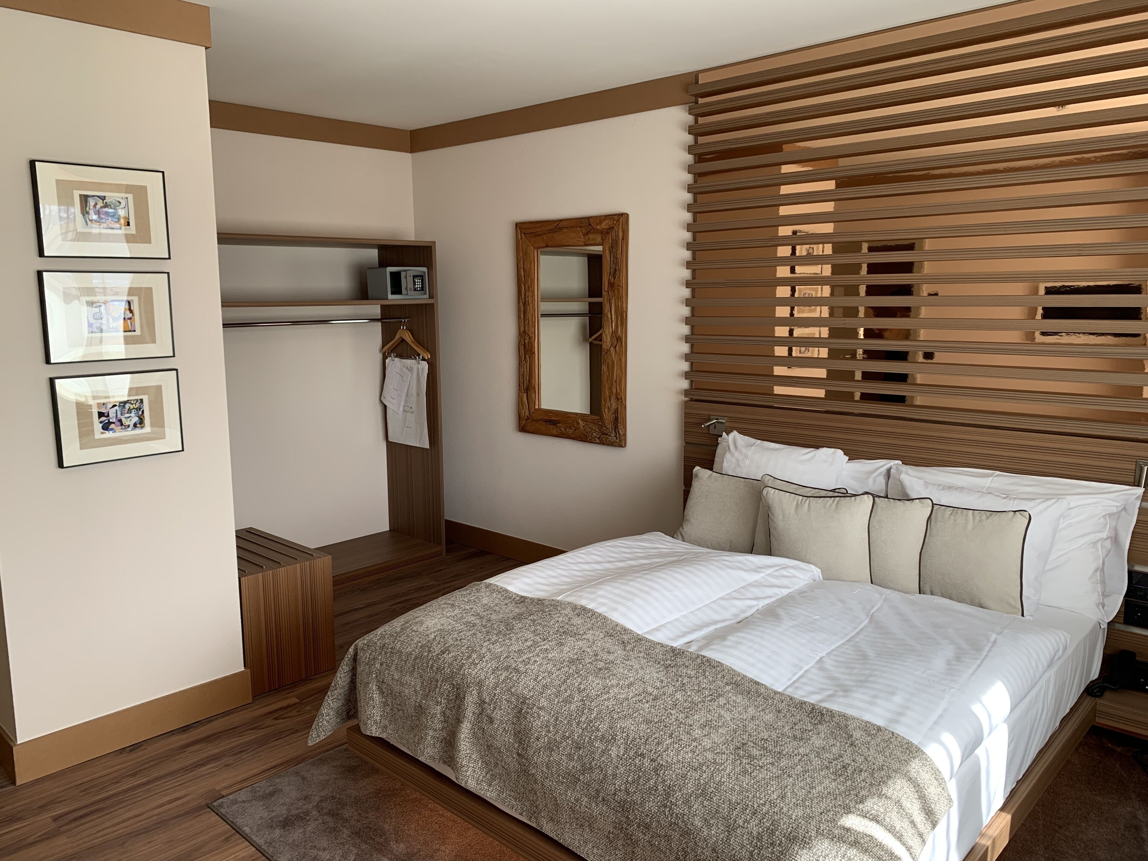 Un dormitorio con cama, persianas de madera, un espejo y cuadros en la pared.