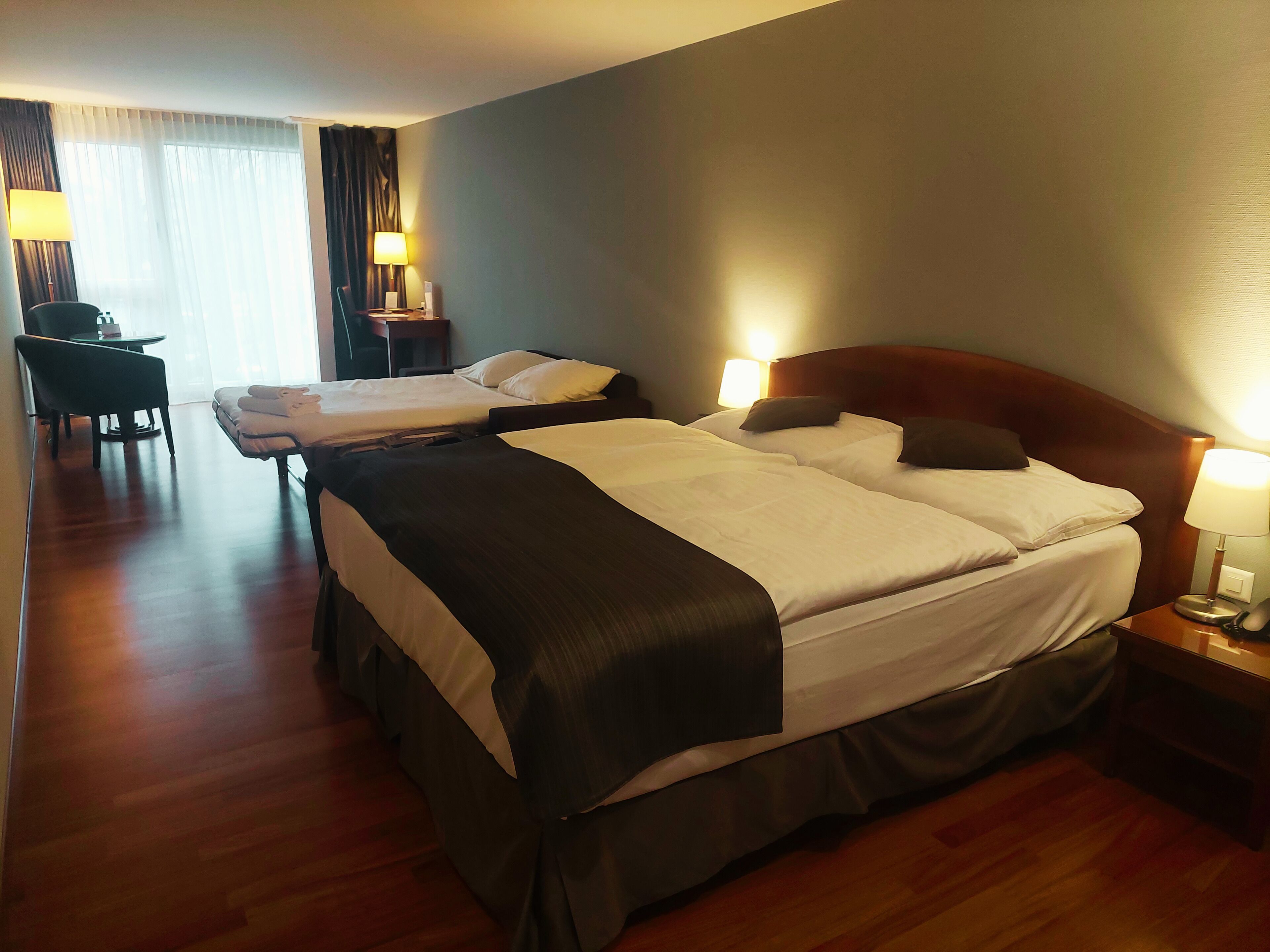 Une chambre d’hôtel avec deux lits, un bureau, une chaise et une lampe.