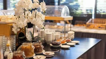 Ein reichhaltiges Buffet mit verschiedenen Speisen, darunter Gläser mit Marmelade und eine Anordnung weißer Blumen.