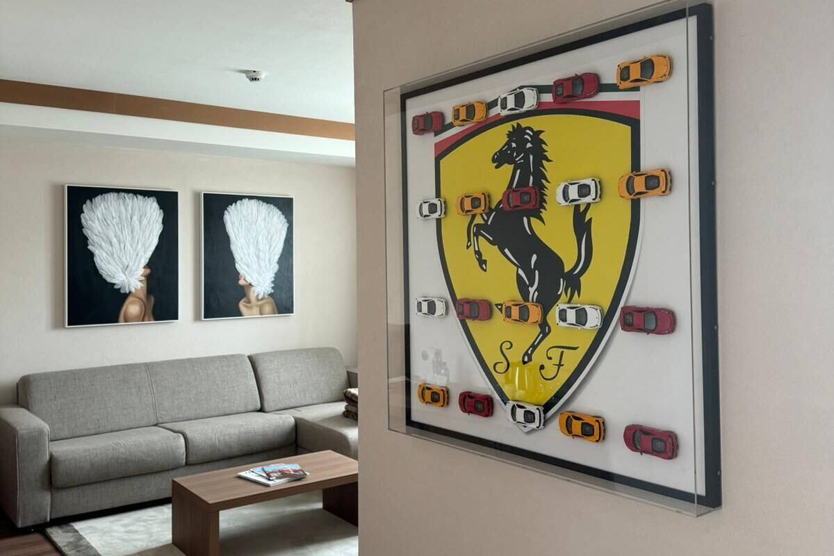 A living room with a grey sofa, a coffee table, and a framed Ferrari logo on the wall.