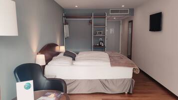 A hotel room with a bed, a desk, a chair, a lamp, a shelf with toiletries, and a TV on the wall.