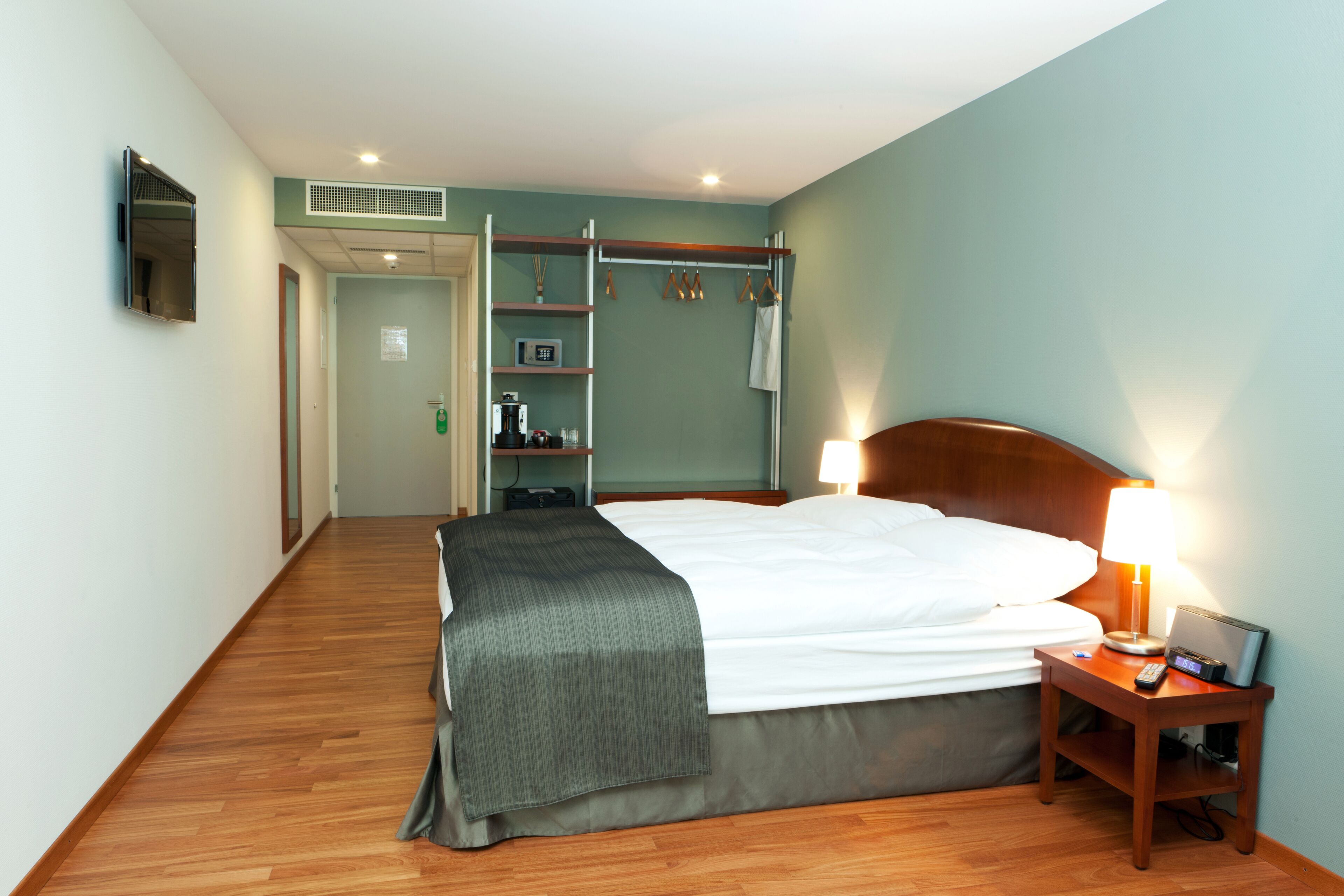 Habitación de hotel con cama, mesita de noche, lámpara y suelo de madera.